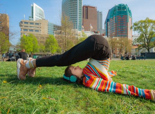 Meisje in gekleurde trui in yoga-houding met Den Haag als achtergrond